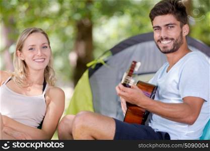 young couple with guitar outside tent
