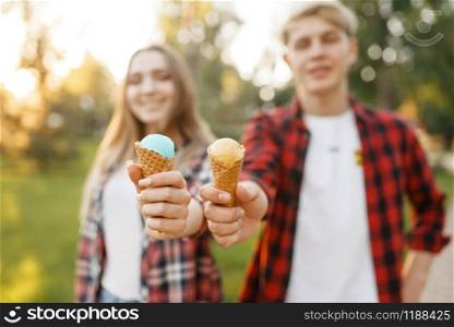 Young couple with ice cream walking in summer park. Boyfriend and girlfriend leisures with ice-cream