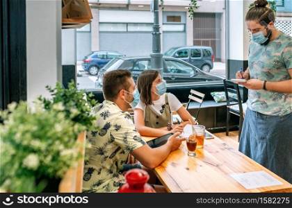 Young couple with mask making food order to waiter with mask too. Couple with mask making food order to waiter