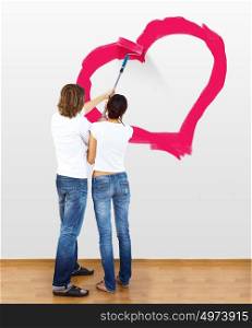 Young couple with paint brushes drawing heart on the wall