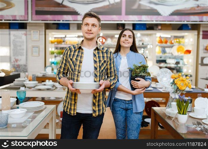 Young couple with plates in houseware store. Man and woman buying home goods in market, family in kitchenware supply shop. Young couple with plates in houseware store