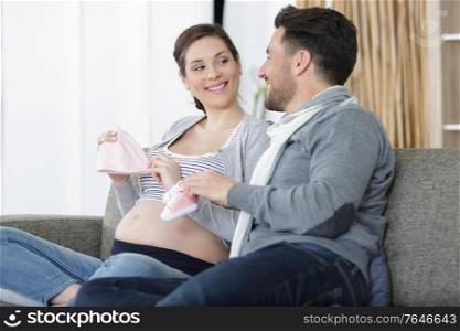 young couple with pregnant woman holding children clothes