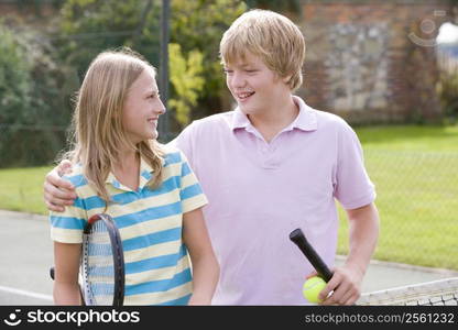 Young couple with rackets on tennis court smiling