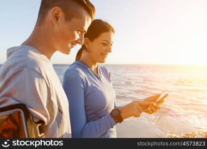 Young couple with smartphones outdoors. Two young people in sport wear with smartphones outdoors