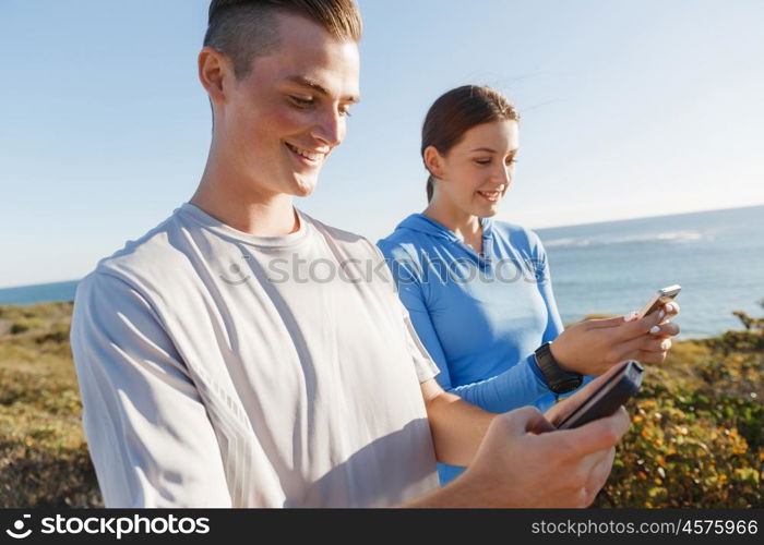 Young couple with smartphones outdoors. Two young people in sport wear with smartphones outdoors