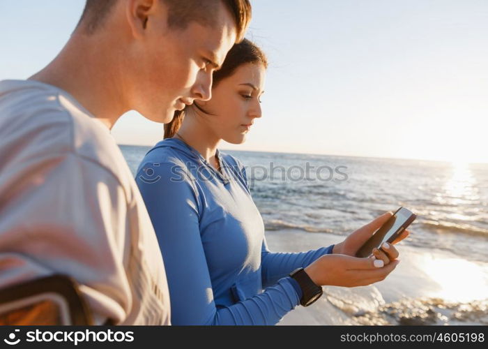 Young couple with smartphones outdoors. Two young people in sport wear with smartphones outdoors