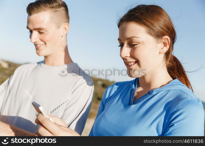 Young couple with smartphones outdoors. Two young people in sport wear with smartphones outdoors