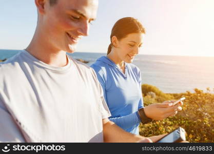 Young couple with smartphones outdoors. Two young people in sport wear with smartphones outdoors