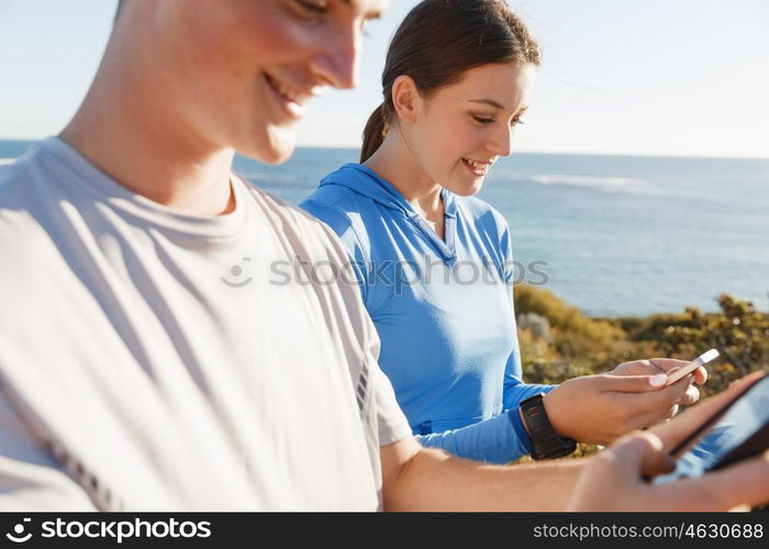 Young couple with smartphones outdoors. Two young people in sport wear with smartphones outdoors