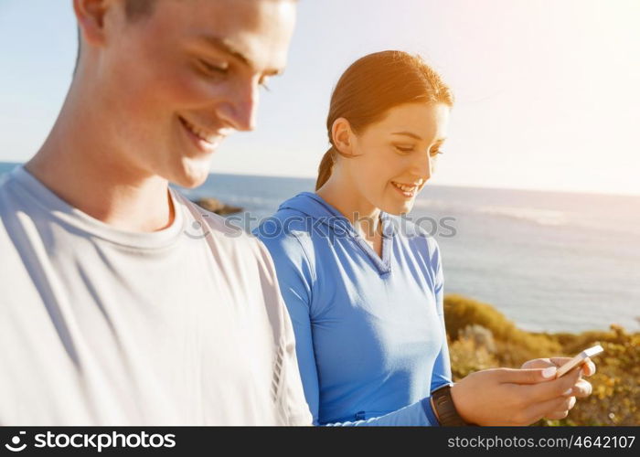 Young couple with smartphones outdoors. Two young people in sport wear with smartphones outdoors