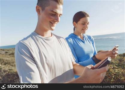 Young couple with smartphones outdoors. Two young people in sport wear with smartphones outdoors