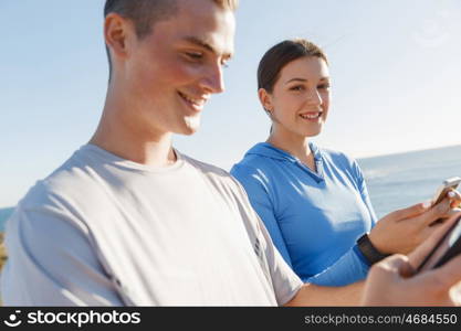 Young couple with smartphones outdoors. Two young people in sport wear with smartphones outdoors