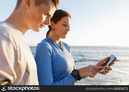 Young couple with smartphones outdoors. Two young people in sport wear with smartphones outdoors