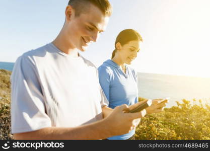 Young couple with smartphones outdoors. Two young people in sport wear with smartphones outdoors