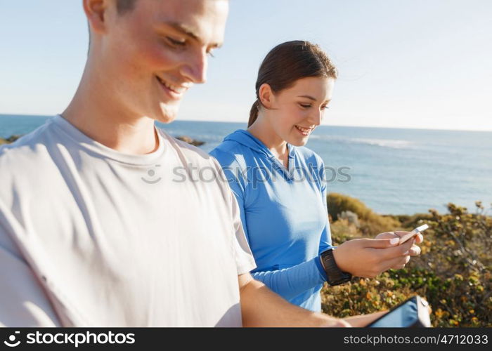 Young couple with smartphones outdoors. Two young people in sport wear with smartphones outdoors