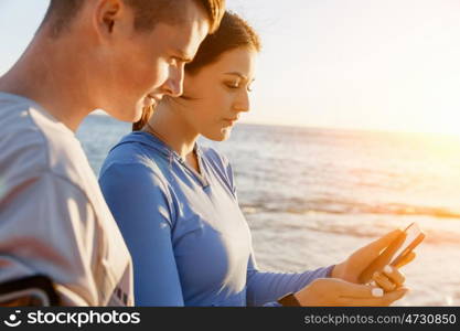 Young couple with smartphones outdoors. Two young people in sport wear with smartphones outdoors