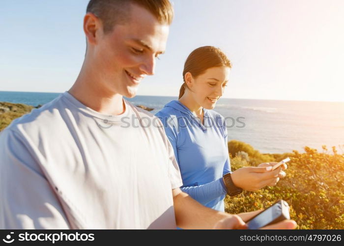 Young couple with smartphones outdoors. Two young people in sport wear with smartphones outdoors