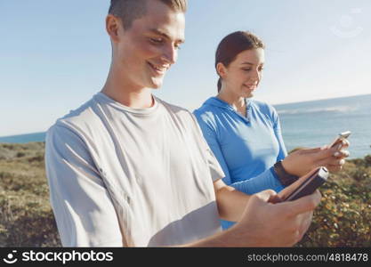 Young couple with smartphones outdoors. Two young people in sport wear with smartphones outdoors