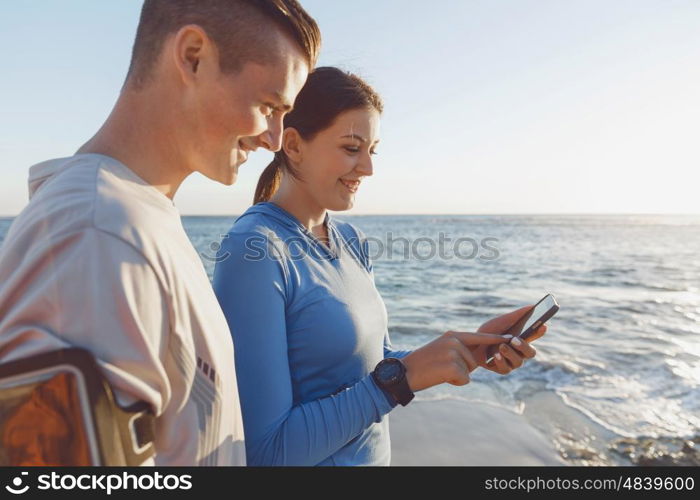 Young couple with smartphones outdoors. Two young people in sport wear with smartphones outdoors