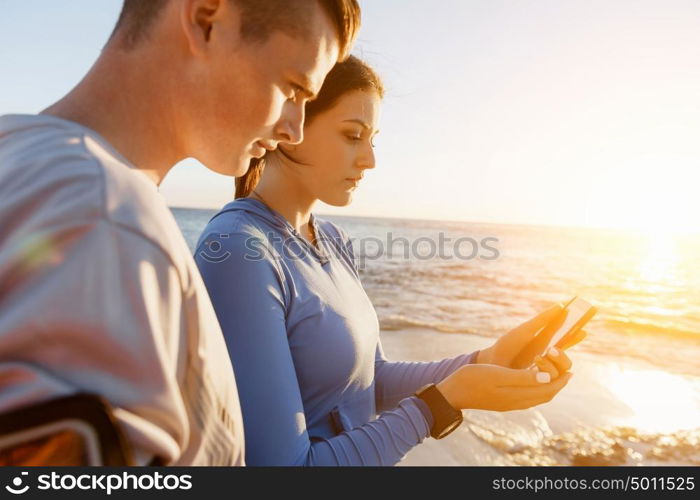 Young couple with smartphones outdoors. Two young people in sport wear with smartphones outdoors