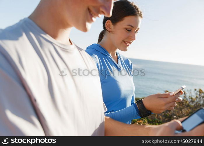 Young couple with smartphones outdoors. Two young people in sport wear with smartphones outdoors