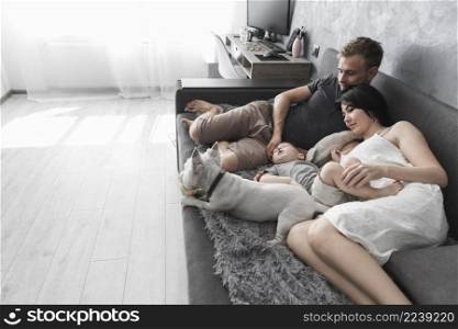 young couple with their son white dog lying grey sofa home