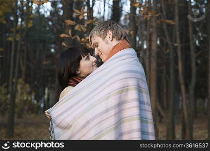Young couple wrapped in blanket, embracing in forest