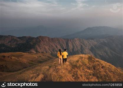 Young couples hiking traveller yellow shirts standing at the middle of a golden meadow mountain view. At Mulayit Taung in Myanmar.