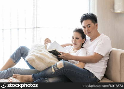 Young Couples reading book tohether in living room of contemporary house for lifestyle concept