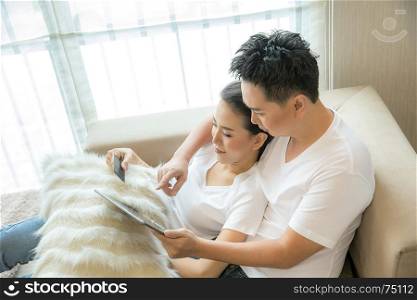 Young Couples using tablet to shopping with credit card in living room of contemporary house for modern lifestyle and e-commerce concept
