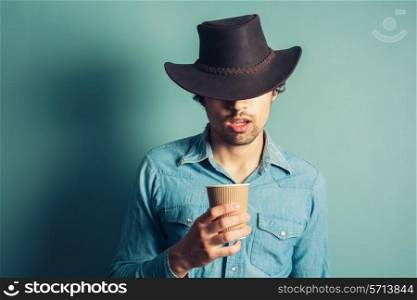 Young cowboy is drinking coffee from a paper cup