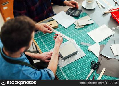 Young craftsman passing metal ruler to friend in print studio, elevated view