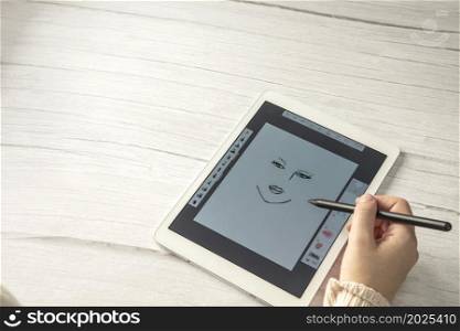 Young creative designer holding stylus pen drawing on screen of digital tablet on wooden desk with copy space, modern digital art top view space for text. Young creative designer holding stylus pen drawing on screen of digital tablet on wooden desk with copy space, modern digital art top view