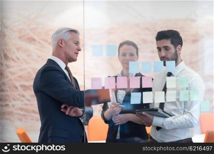 young creative startup business people on meeting with older senior mature businessman at modern office making plans and projects with post stickers on glass