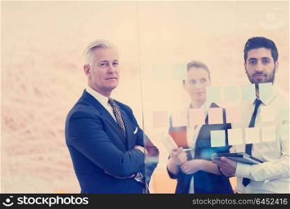 young creative startup business people on meeting with older senior mature businessman at modern office making plans and projects with post stickers on glass