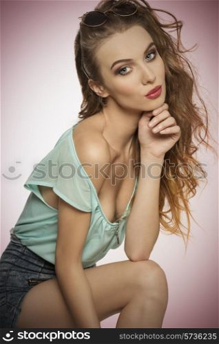 young curly female in fashion pose looking in camera with charming expression, wearing denim shorts, blue shirt and vintage sunglasses on the head. Casual sexy clothes, stylish make-up.