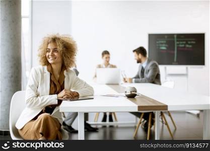 Young curly hair businesswoman using digital tablet in the office with young people works behind her