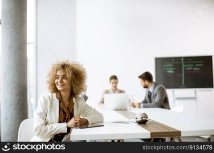 Young curly hair businesswoman using digital tablet in the office with young people works behind her