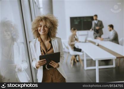 Young curly hair businesswoman using digital tablet in the office with young people works behind her