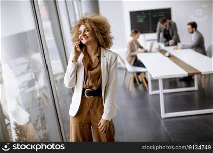 Young curly hair businesswoman using mobile phone in the office with young people works behind her
