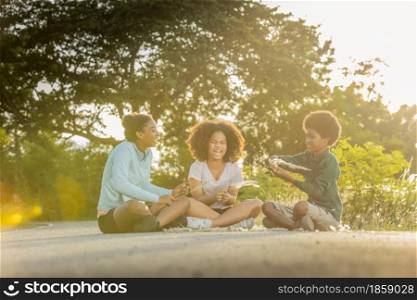 Young curly-haired African American teenger sitting on street and playing hay flowers at sunset time.