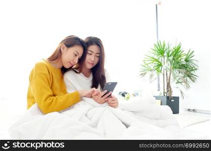 Young cute asia lesbian couple using smart phone with happiness on white bed, lgbt, homosexual, lesbian couple lifestyle
