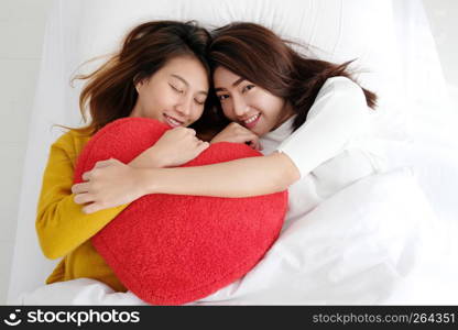 Young cute asia lesbians holding red heart shape willow together lying and smiling with happiness on white bed, LGBT, couple lesbians, valentine?s day concept