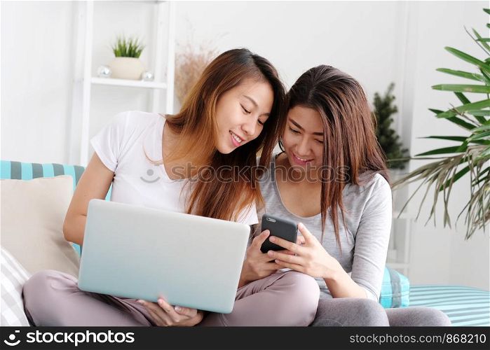 Young cute asian lesbian couple using laptop computer and smart phone with happiness at home, lgbt, homosexual, lesbian couple lifestyle