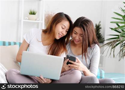 Young cute asian lesbian couple using laptop computer and smart phone with happiness at home, lgbt, homosexual, lesbian couple lifestyle