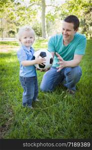 Young Cute Boy and Dad Playing with Soccer Ball in the Park.