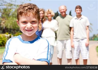 Young cute boy in focus, smailing at camera, with family in the background