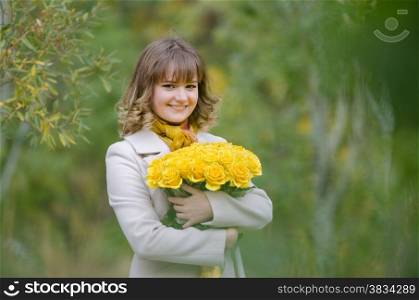 Young cute girl with a bouquet of yellow roses in autumn cool weather