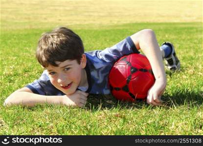 Young cute happy boy lying on grass with red soccer ball