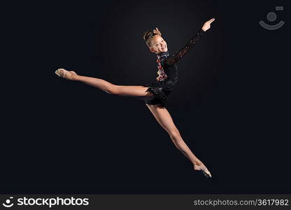 Young cute woman in gymnast suit show athletic skill on black background